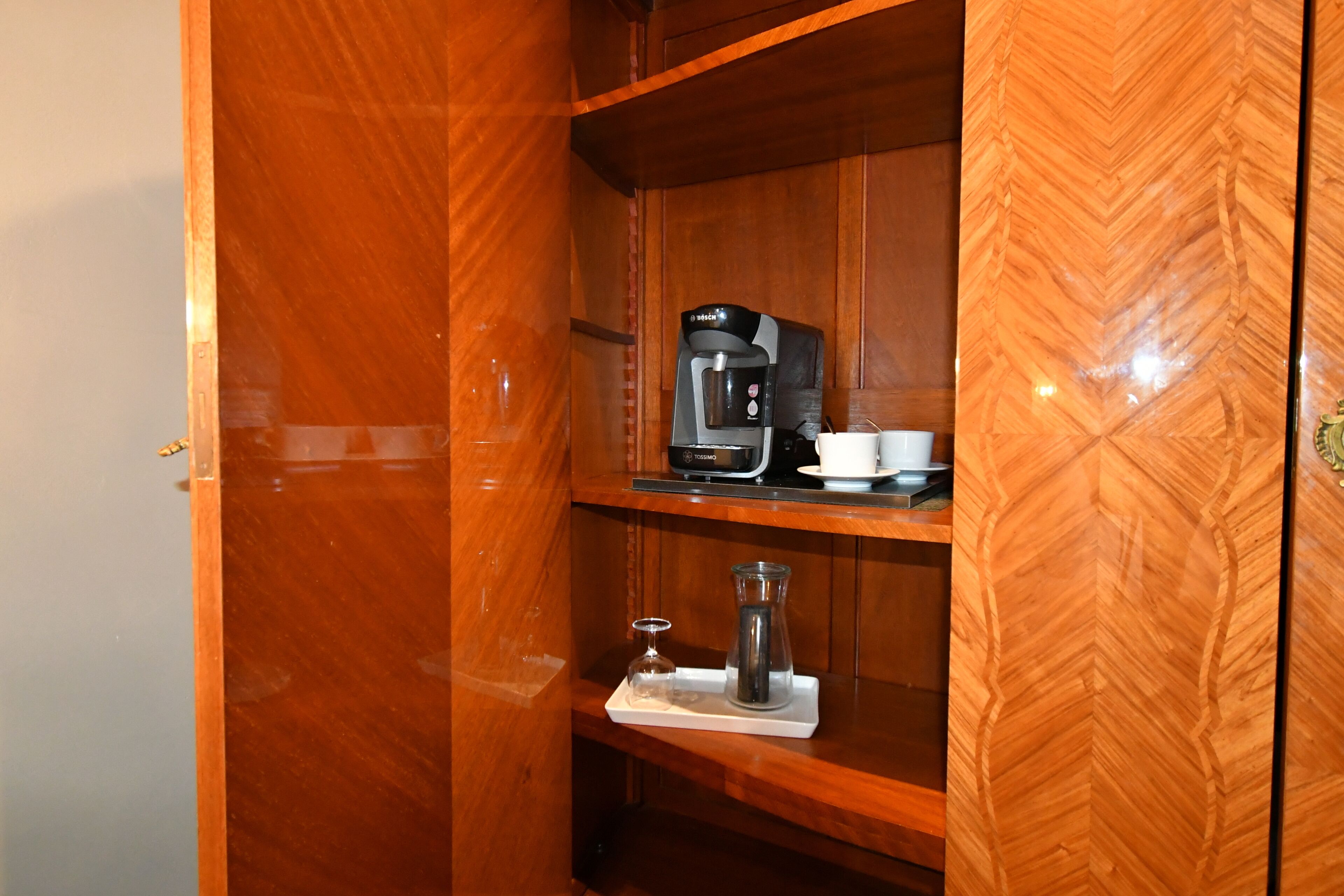 Een houten kastje met een koffiezetapparaat, een kop en een glazen kan op een dienblad.