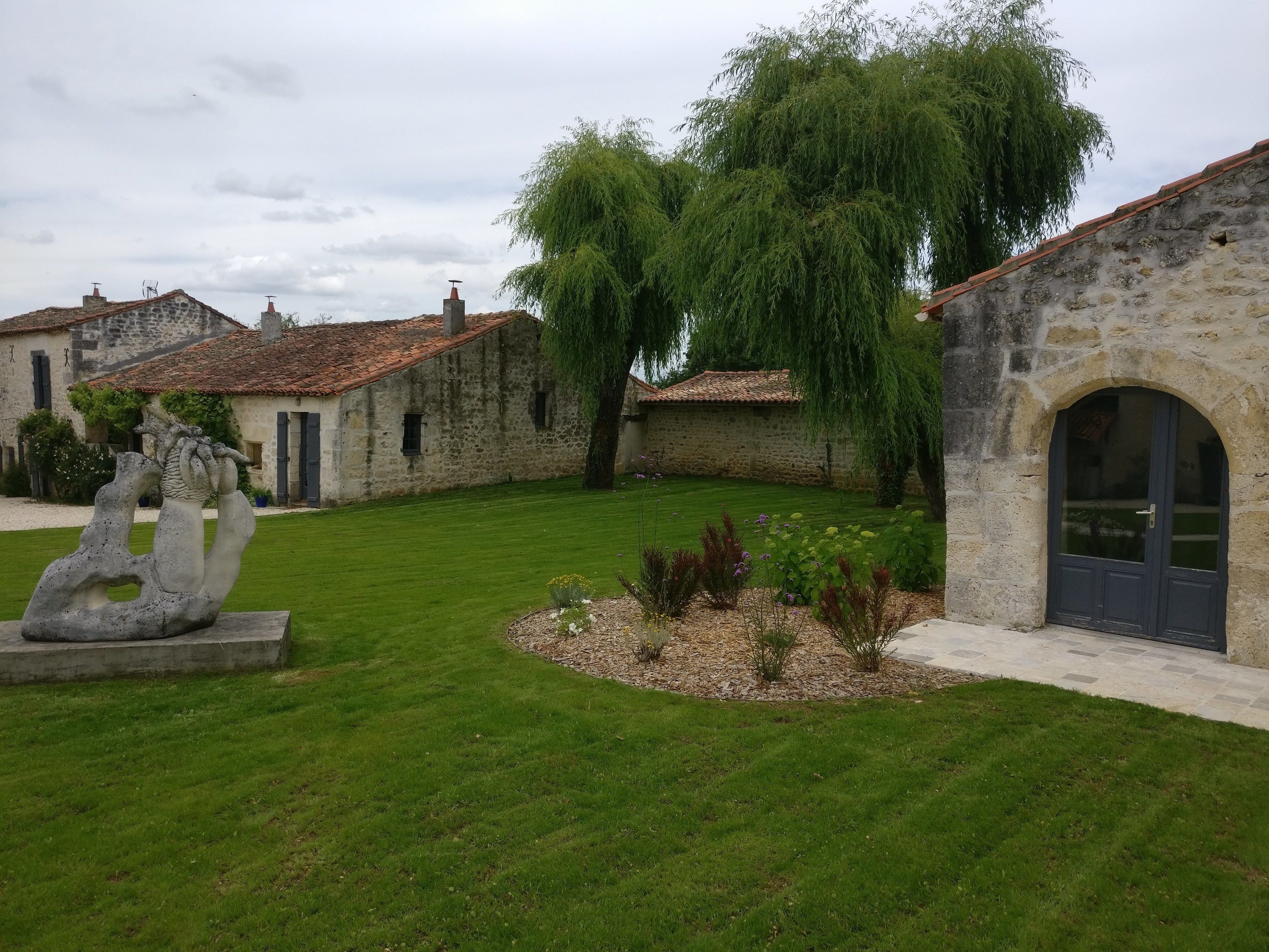 Un patio con edificios de piedra, una escultura y un césped bien cuidado.