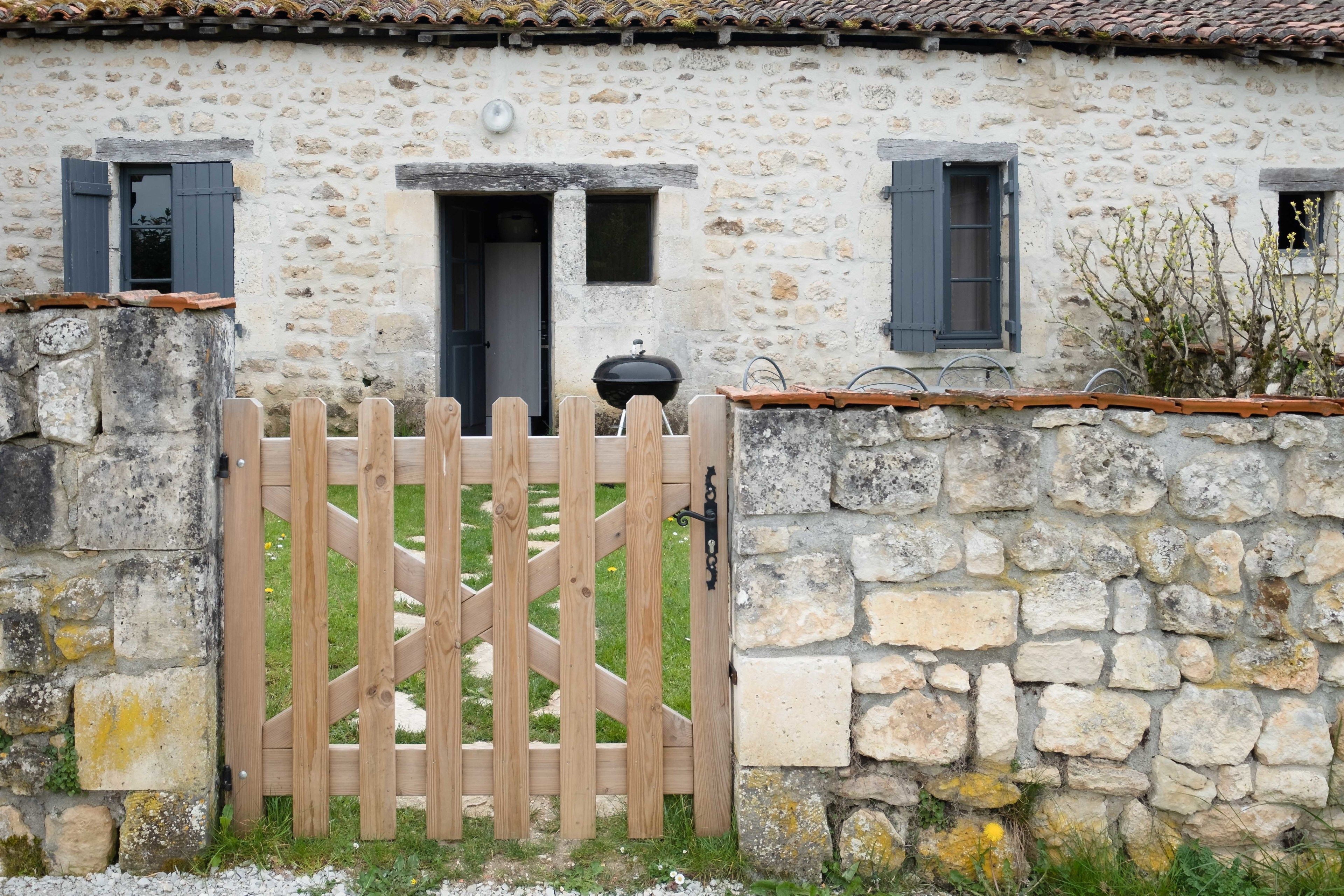 Un edificio de piedra con un portón de madera, una puerta y dos ventanas con contraventanas.