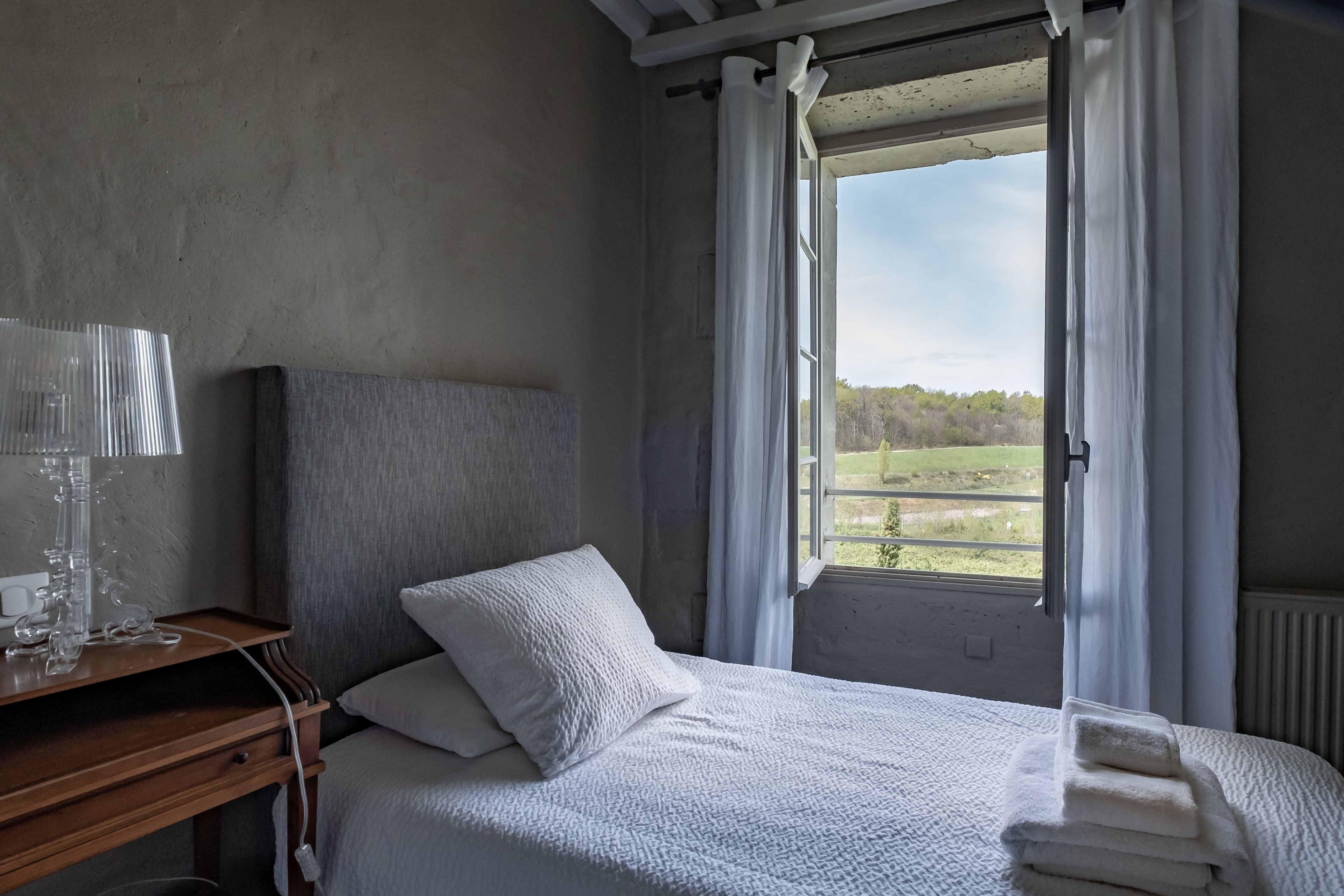 A bedroom with a bed, a bedside table, and a window with curtains.