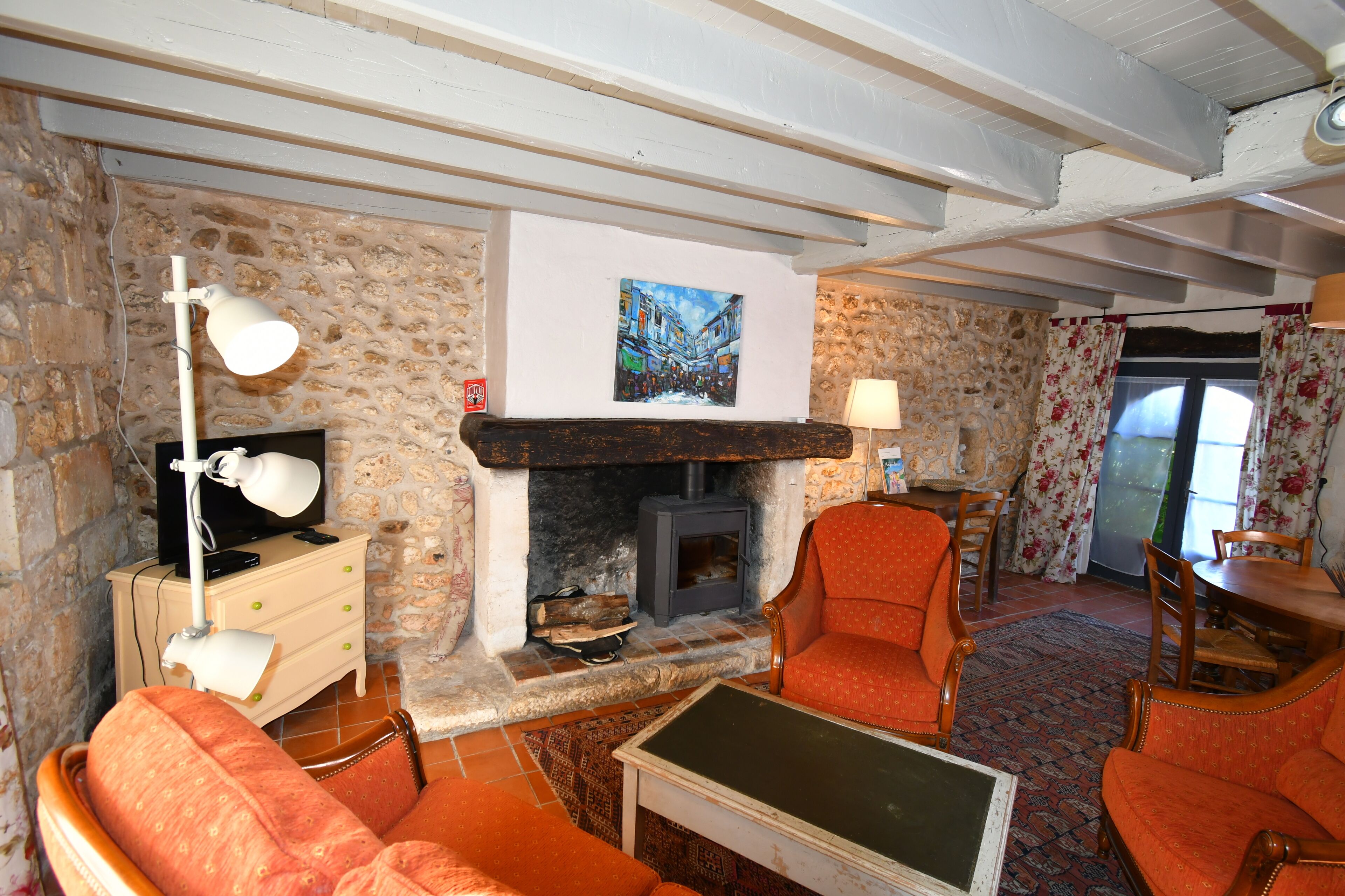 Een gezellige woonkamer met een stenen muur, een open haard, oranje fauteuils, een houten tafel en een televisie op een dressoir.