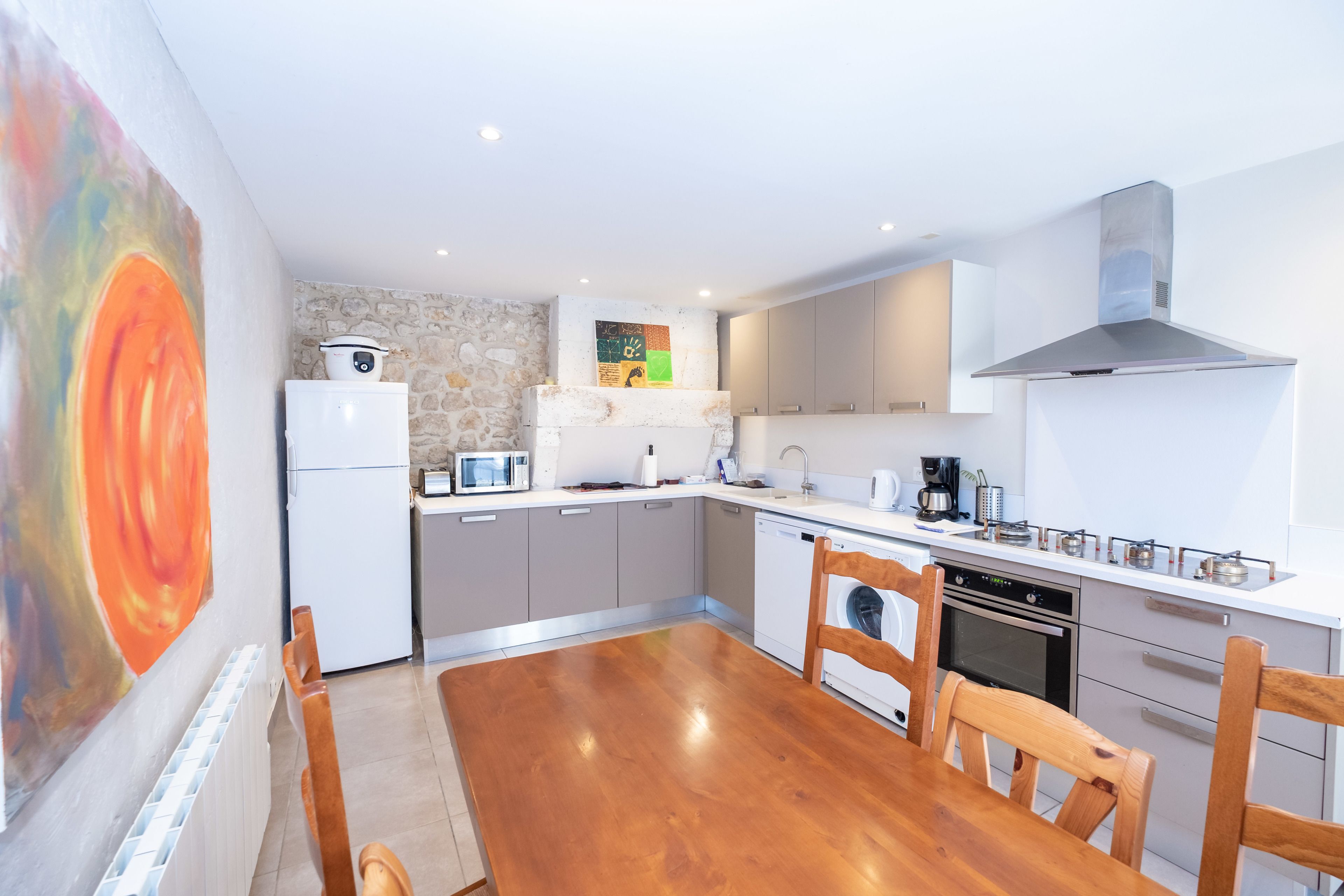 Een moderne keuken met witte apparaten, een accentmuur van steen en een eethoek met houten stoelen.