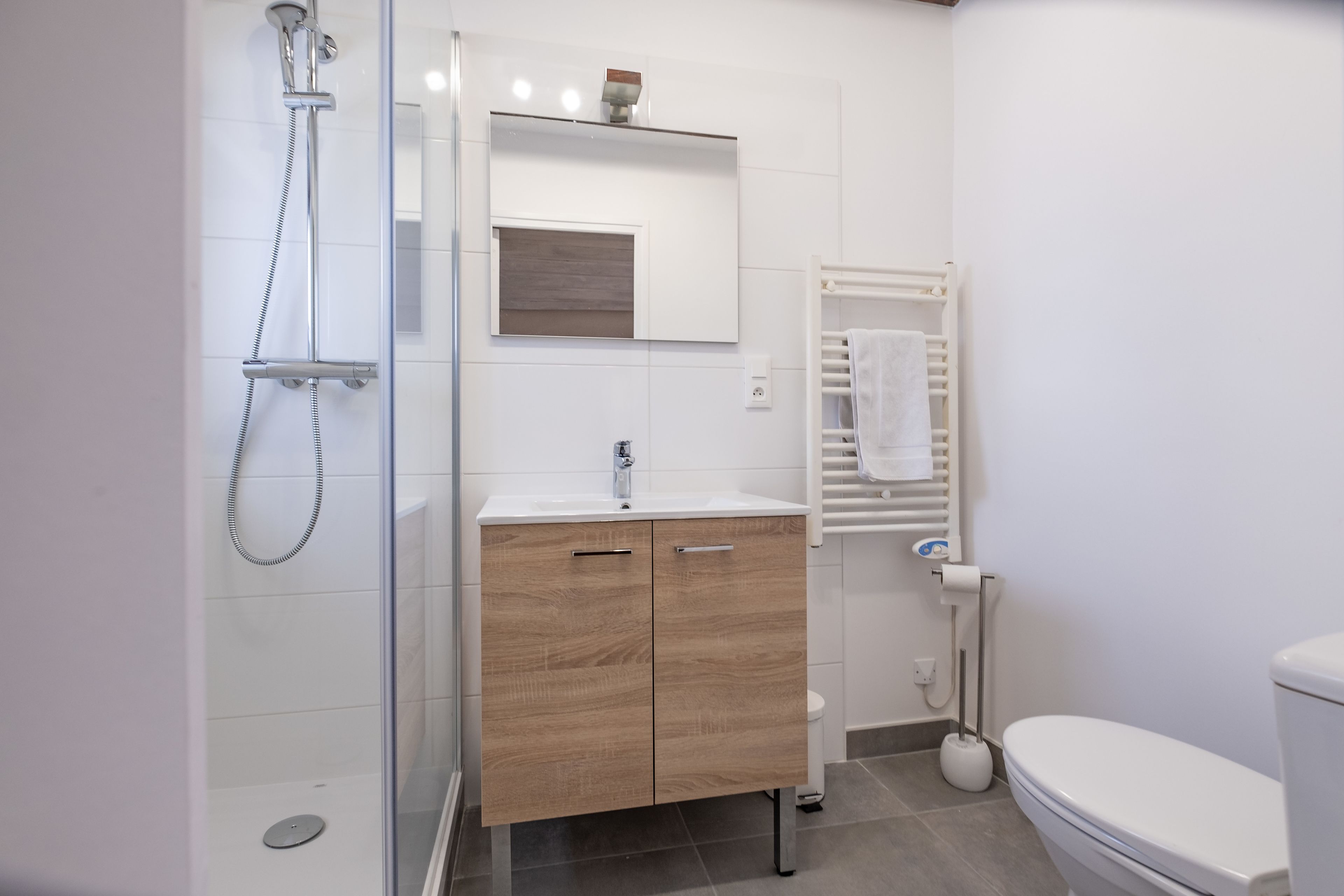 A modern bathroom with a glass shower enclosure, a wooden vanity, a white toilet, and a towel rack.