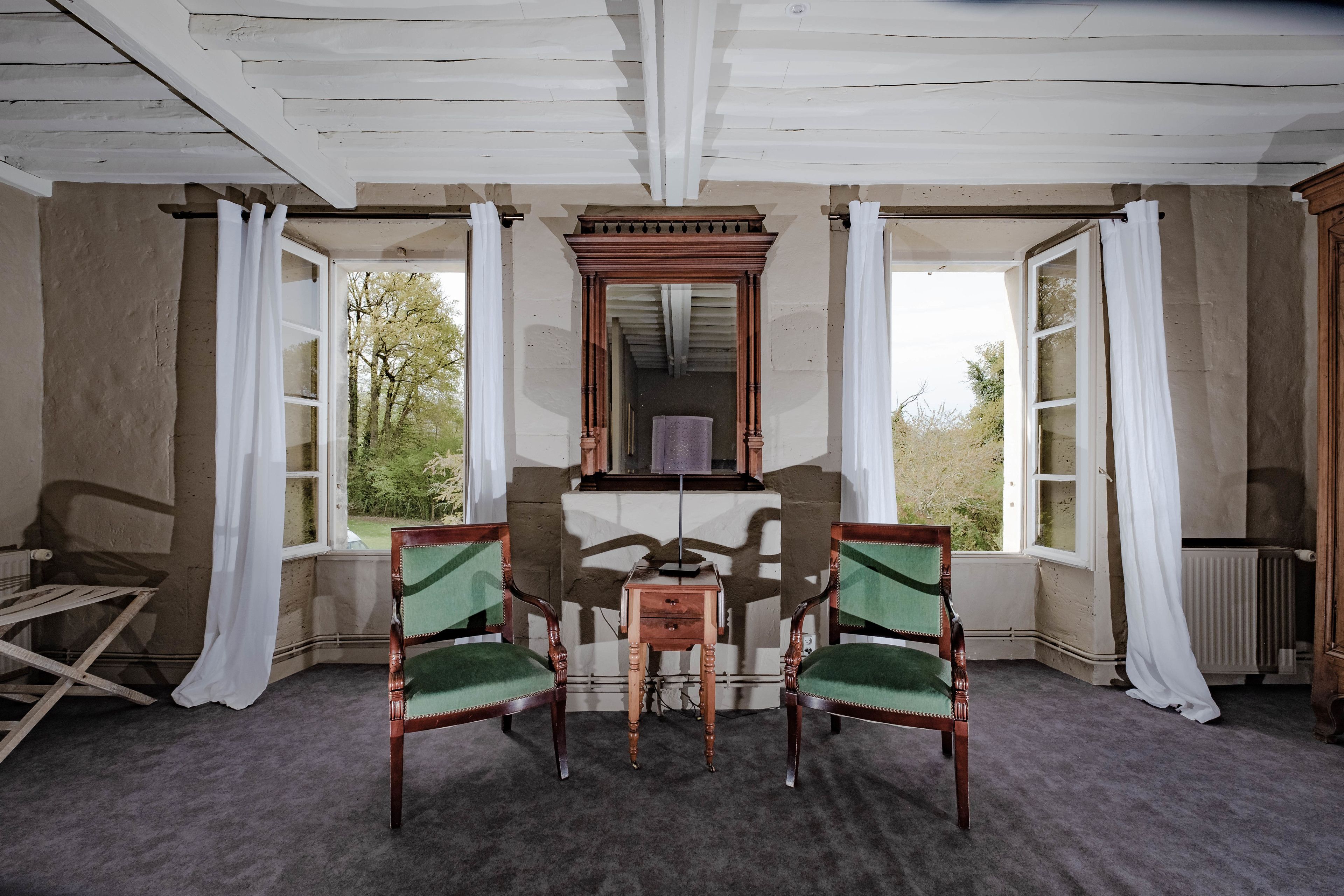 A room with two wooden chairs, a small table, and a mirror on the wall.