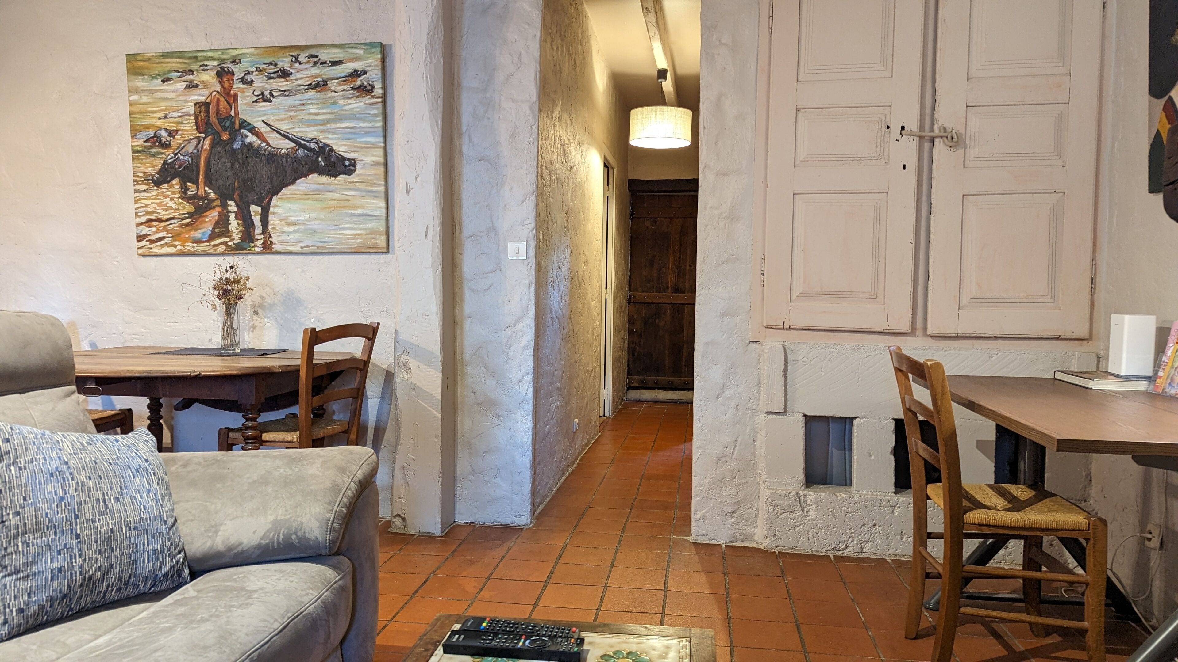 Una sala de estar acogedora con un sofá, una mesa de comedor y sillas. En la pared, un cuadro de una mujer y un toro.