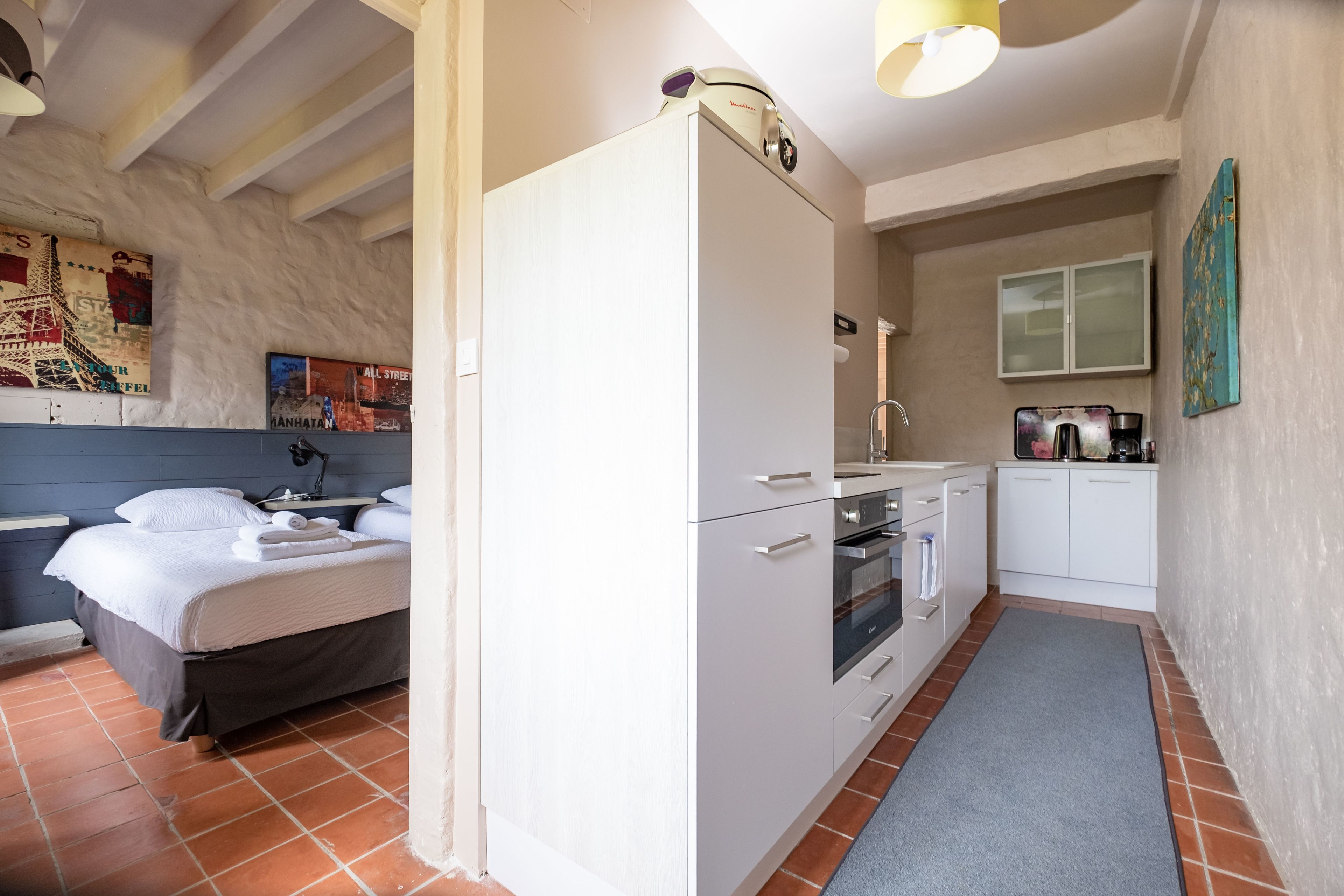A modern bedroom with a bed, a white wardrobe, and a kitchenette with a sink and stove.