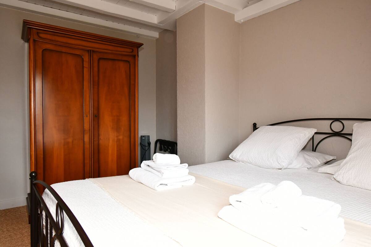 A neatly made bed with white linens and towels, a wooden wardrobe, and a simple headboard.