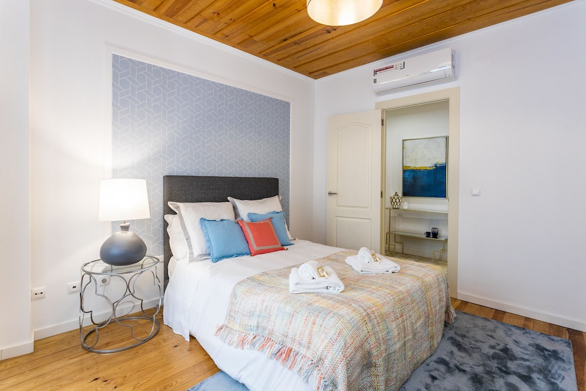 Ein Schlafzimmer mit Bett, Nachttisch mit Lampe, einer Wand mit Muster, einer Tür und einem Deckenventilator.