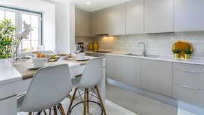 A modern kitchen with grey cabinets, a white countertop, and a dining area with white chairs. - LxWay Poiais de São Bento (Lisbon)