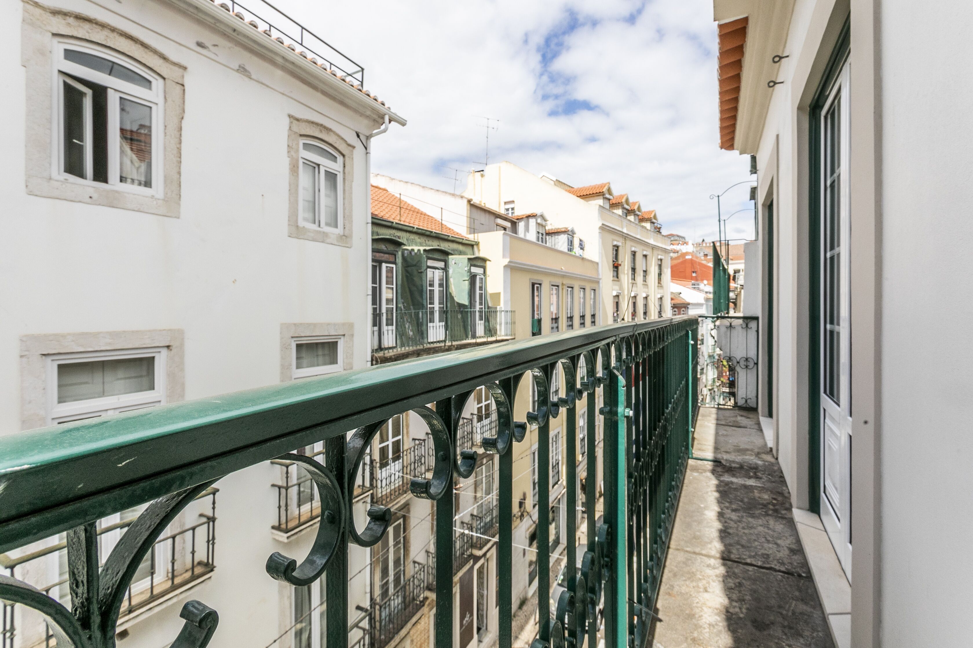 Eine schmale Stadtstraße mit Häusern an beiden Seiten, einem grünen Metallgeländer und blauem Himmel.