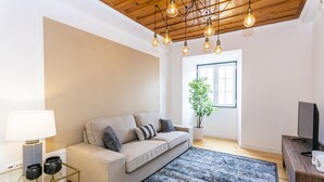 A modern living room with a sofa, a coffee table, a TV stand, and a large window with a plant. - LxWay Poiais de São Bento (Lisbon)
