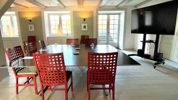 A conference room with a large table, red chairs, and a television on a stand.