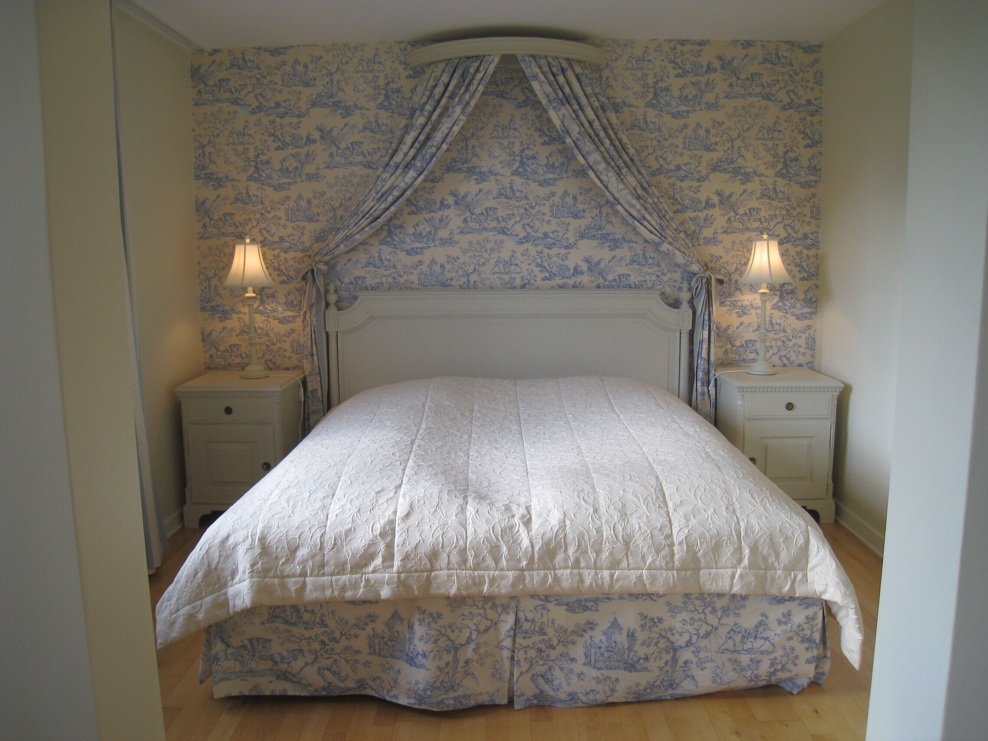 A bedroom with a canopy bed, floral wallpaper, and bedside lamps.