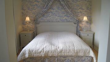 A bedroom with a canopy bed, floral wallpaper, and bedside lamps.
