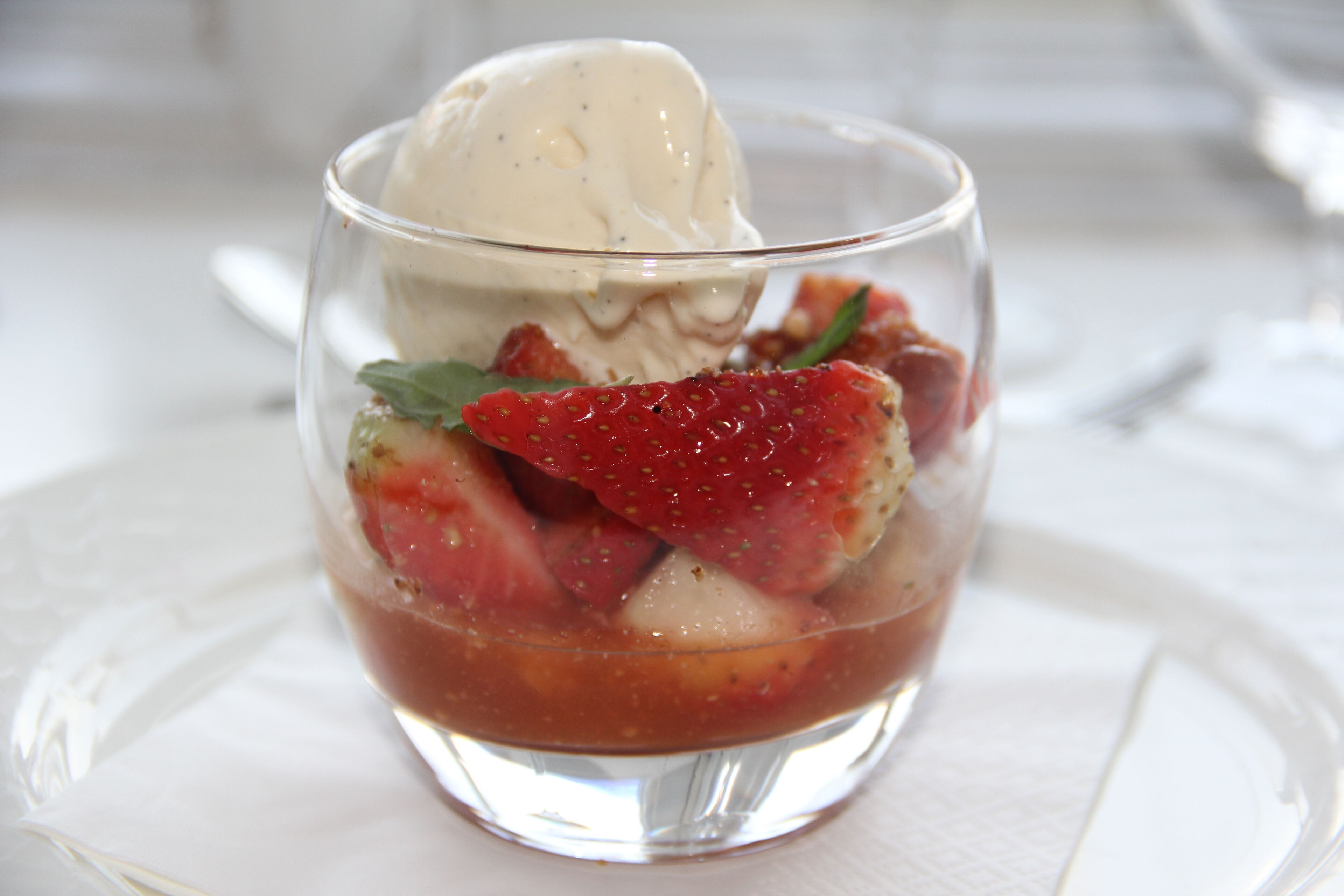 A dessert with ice cream and strawberries in a clear glass.