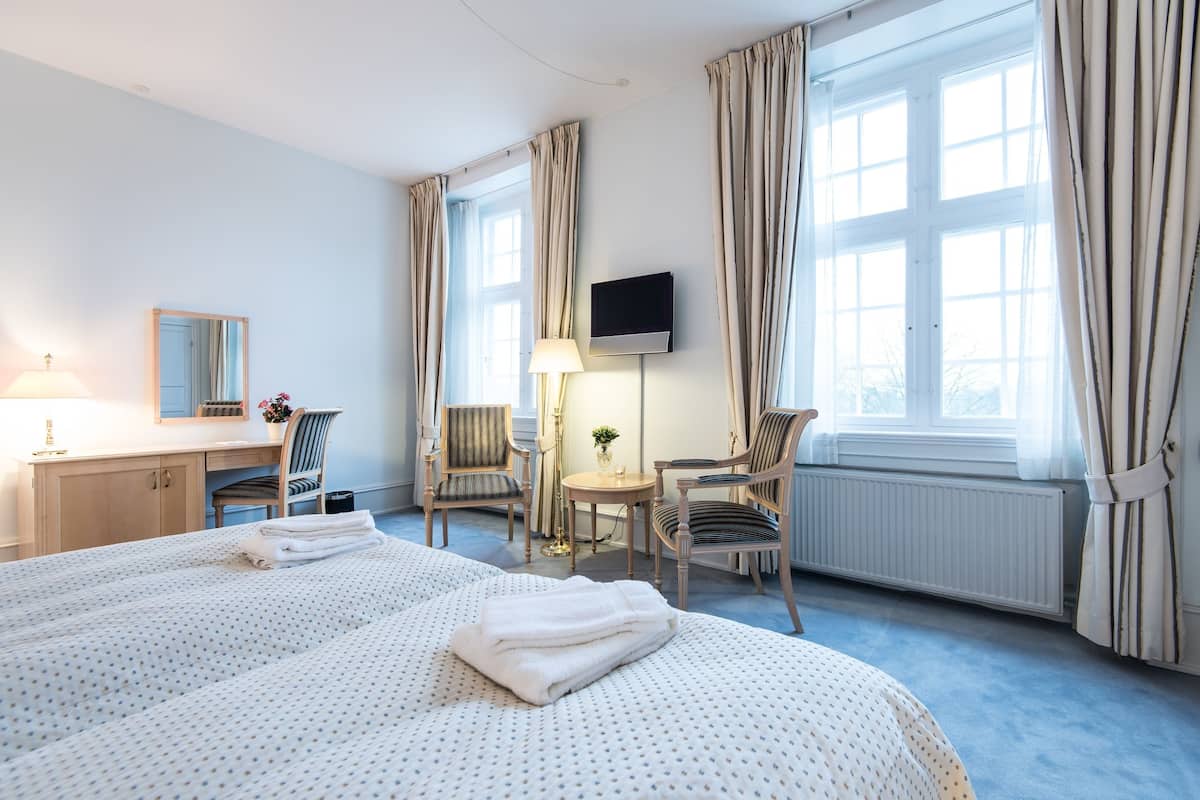 Ett hotellrum med två sängar, ett skrivbord, en stol, en TV och ett fönster med gardiner.