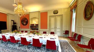 A formal dining room with a long table set for a meal, surrounded by red chairs.