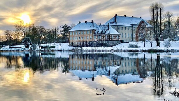 A large building with a reflection in a calm body of water, surrounded by snow-covered trees and a clear sky. - Skjoldenæsholm Hotel og Konferencecenter (Ringsted)
