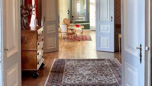 A hallway with a large chandelier, wooden floors, and a patterned rug leading to a dining area. - Skjoldenæsholm Hotel og Konferencecenter (Ringsted)
