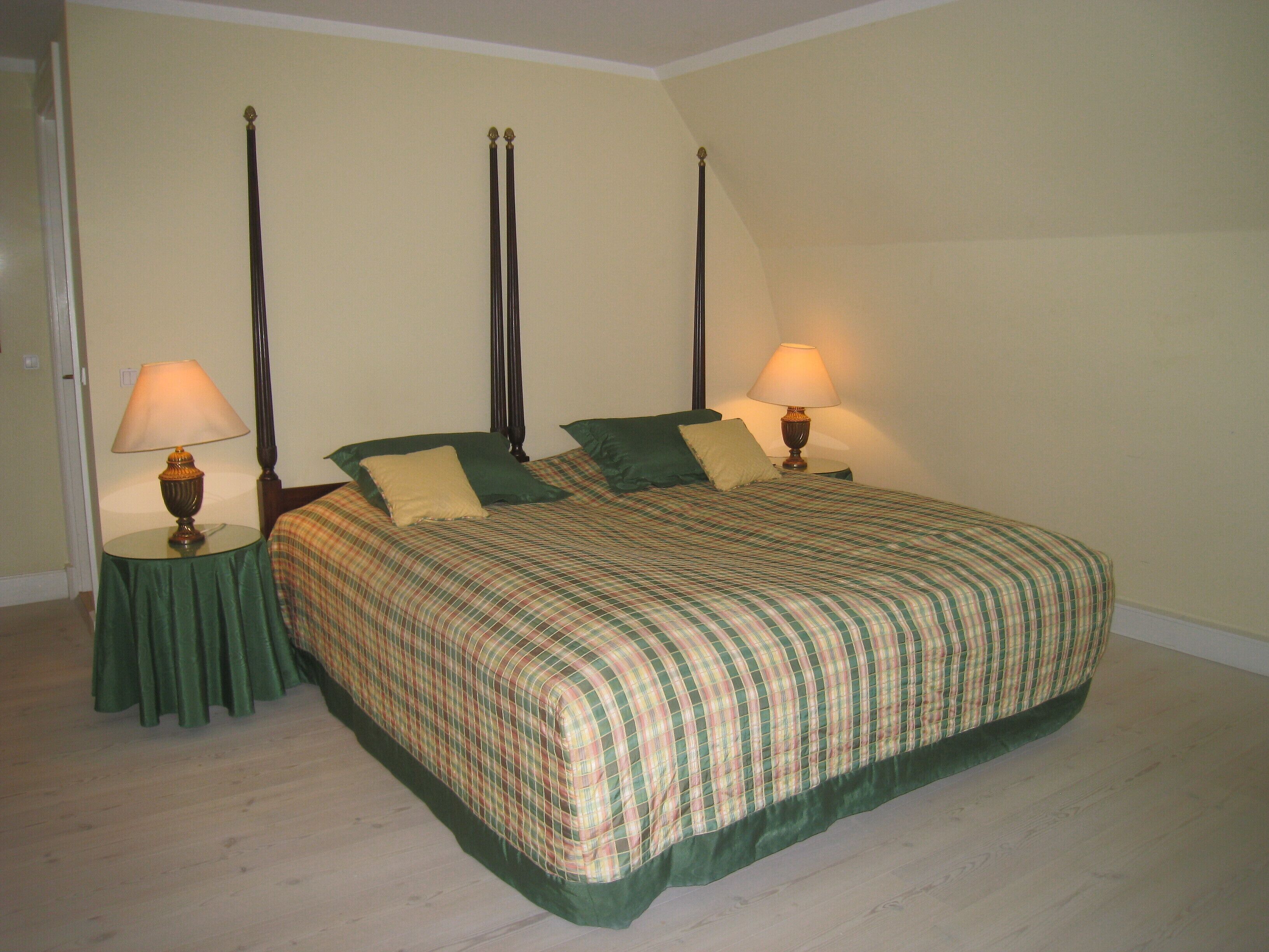 A neatly made bed with a plaid bedspread, two bedside tables with lamps, and a green skirt skirt.