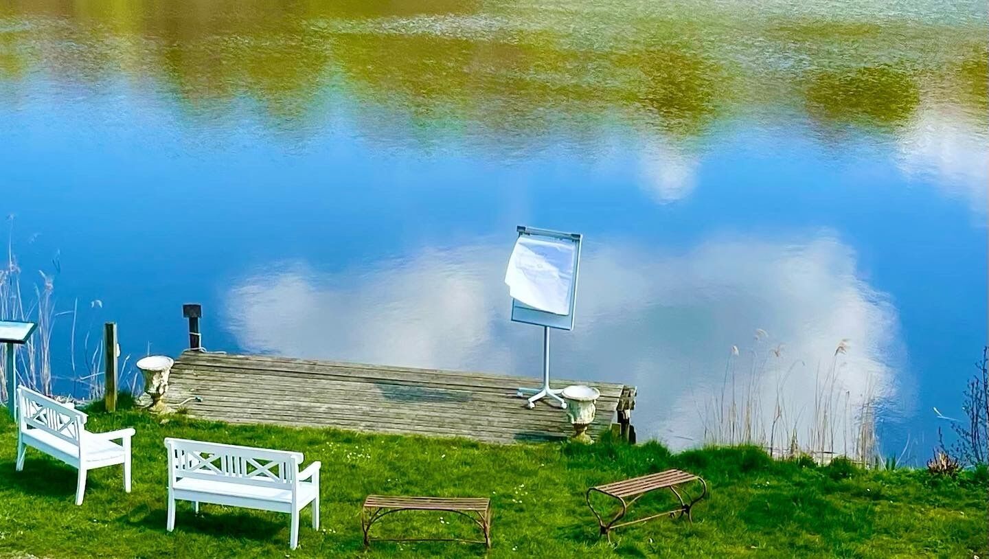 A lakeside setting with a wooden dock, benches, and a signpost.
