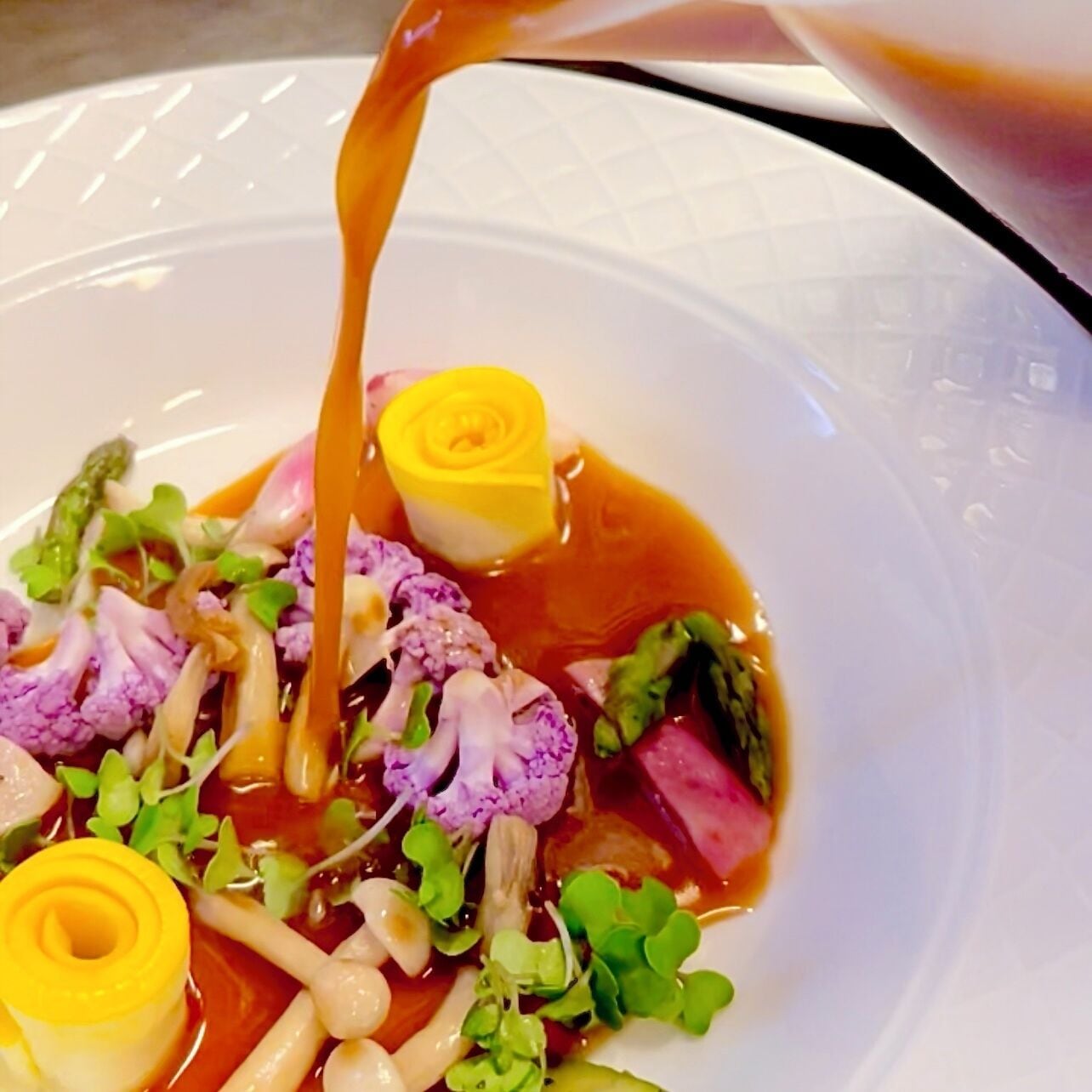 Un plato con una variedad de verduras y una flor amarilla, con salsa vertida encima.
