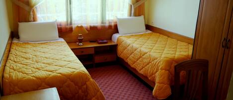 A twin room with two beds, a nightstand, a lamp, and a chair.