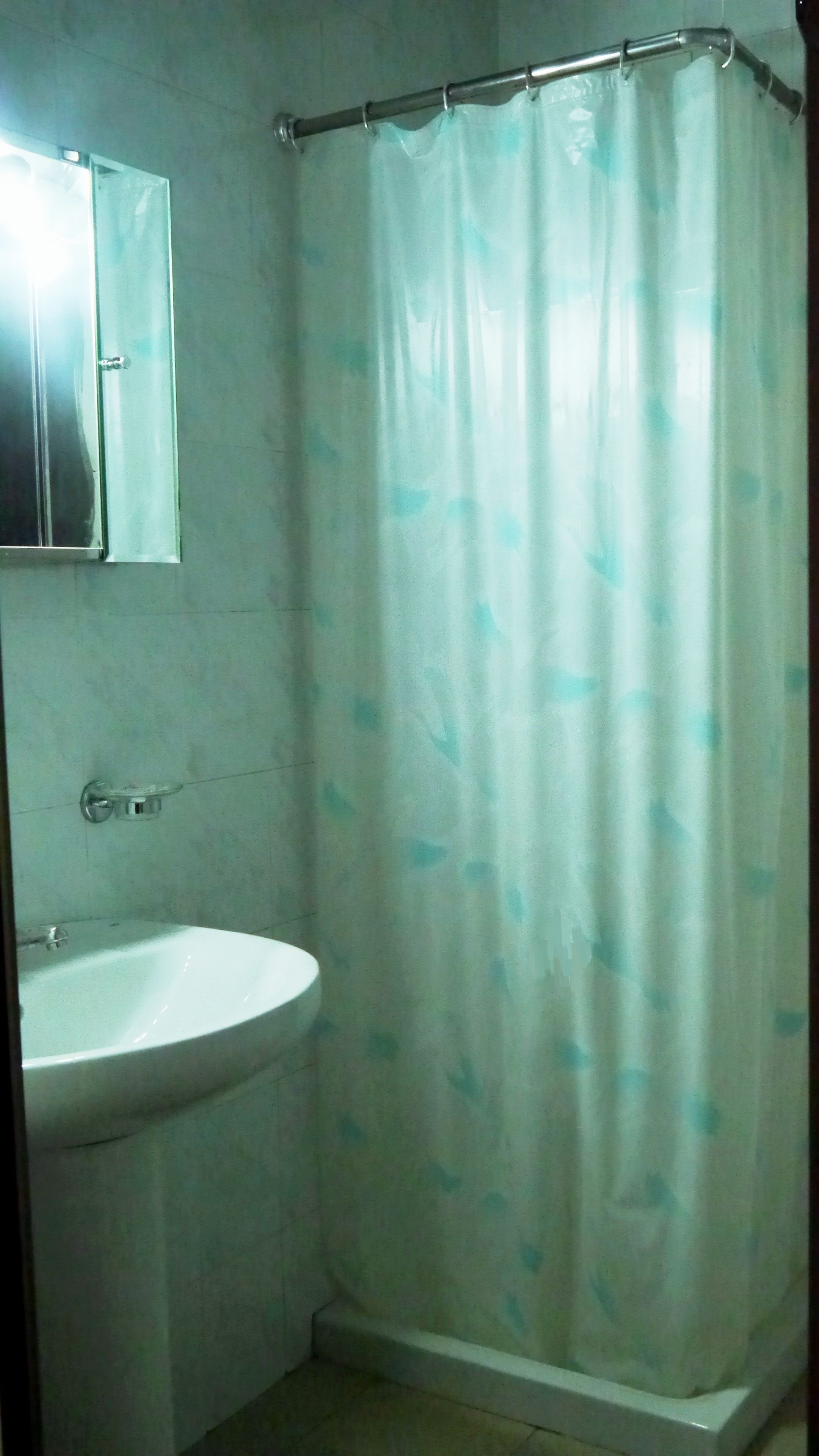 Un baño con un lavabo blanco, un espejo encima y una cortina de ducha estampada.
