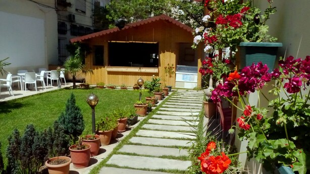 A garden with a patio area, potted plants, and a small building with a red roof. - Hotel Kruja (Tirana)