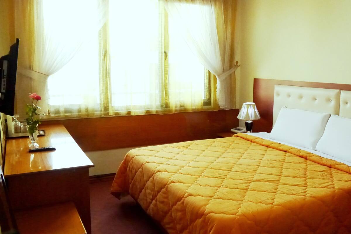 A hotel room with a bed, a desk, a lamp, and a window with curtains.