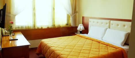 A hotel room with a bed, a desk, a lamp, and a window with curtains.