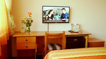 Habitación de hotel con escritorio de madera, televisión montada en la pared, un jarrón con flores, un reloj y una cama con colcha.