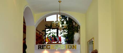 A reception area with a desk, computer, and a sign that reads "RECEPTION". There are potted plants and a glass display case with items.