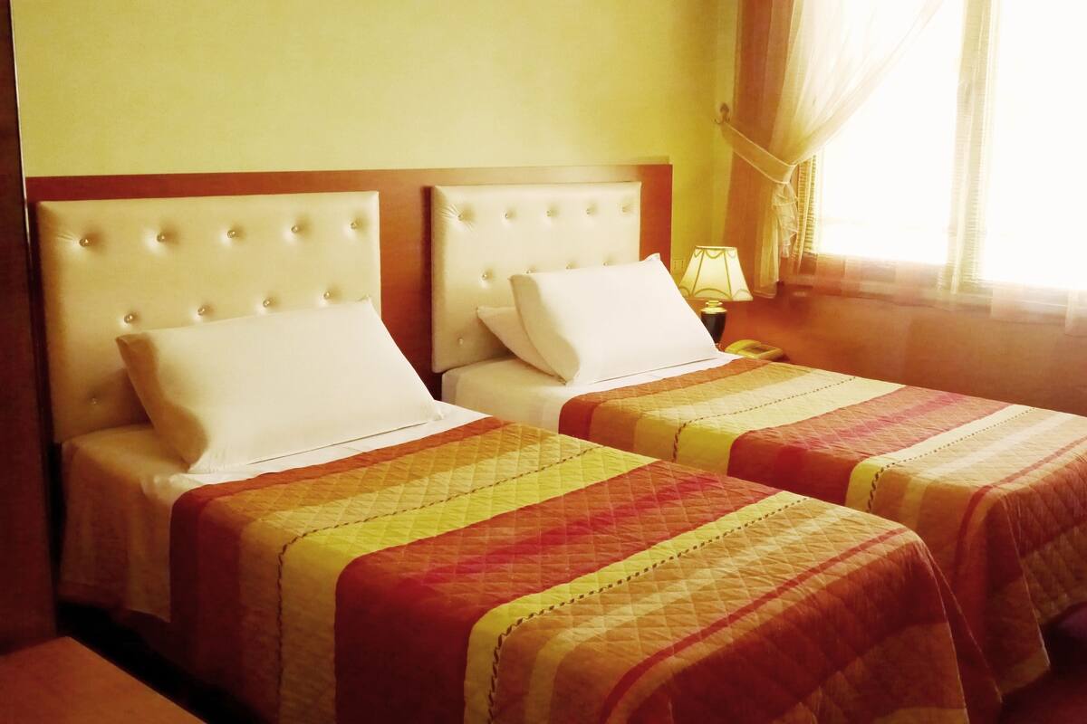 Two beds with headboards, a bedside table, and a window with curtains.
