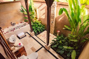 Un baño con bañera, lavamanos e inodoro, rodeado de plantas y un muro de piedra.