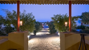 A pathway leading to a beach with a covered area and palm trees. - Prince Desert Camp (Jaisalmer)