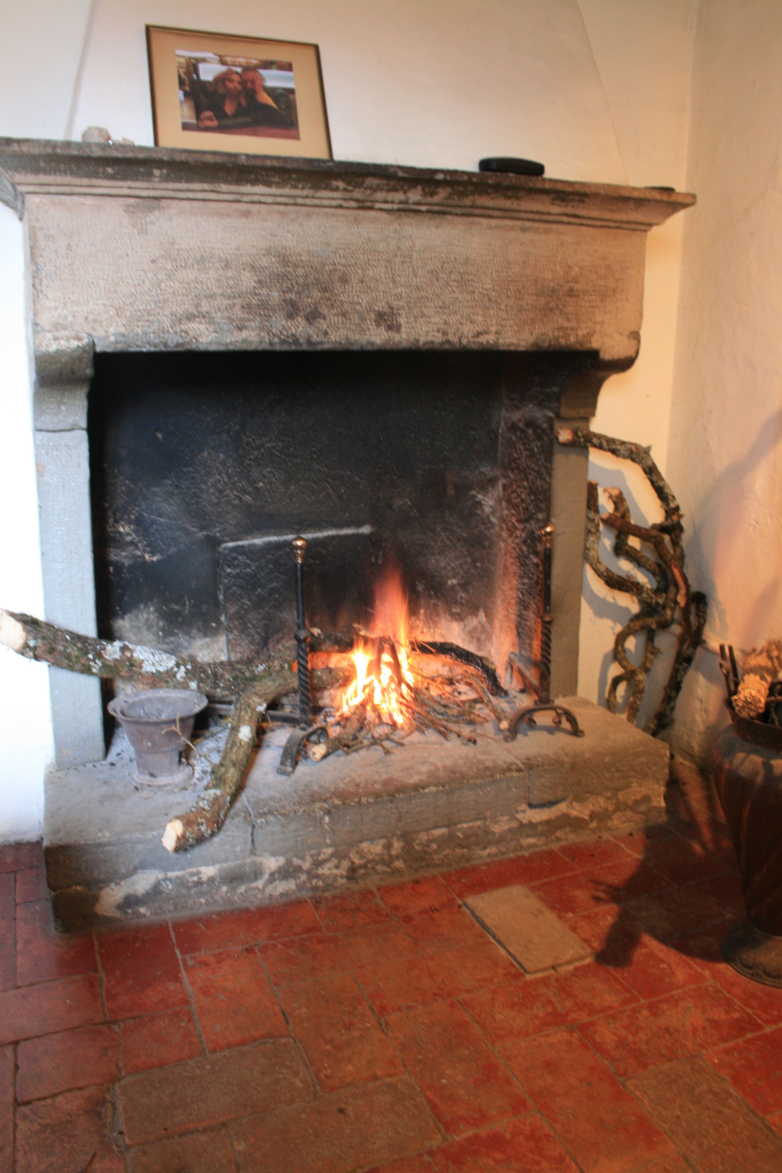 A fireplace with a fire, a framed picture above it, and a brick floor.
