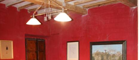 A room with a red wall, a bed with a colorful quilt, a wooden dresser, and a chandelier.