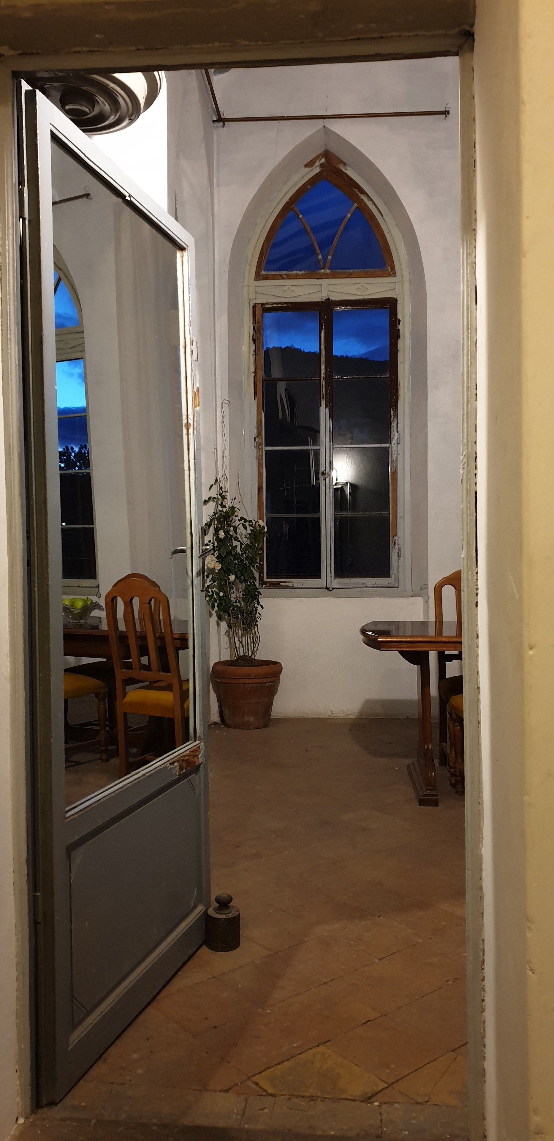 Habitació amb una gran finestra d'arc, una planta en test i una zona de dinar amb cadires i taula.