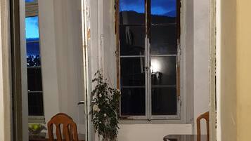 Habitació amb una gran finestra d'arc, una planta en test i una zona de dinar amb cadires i taula.