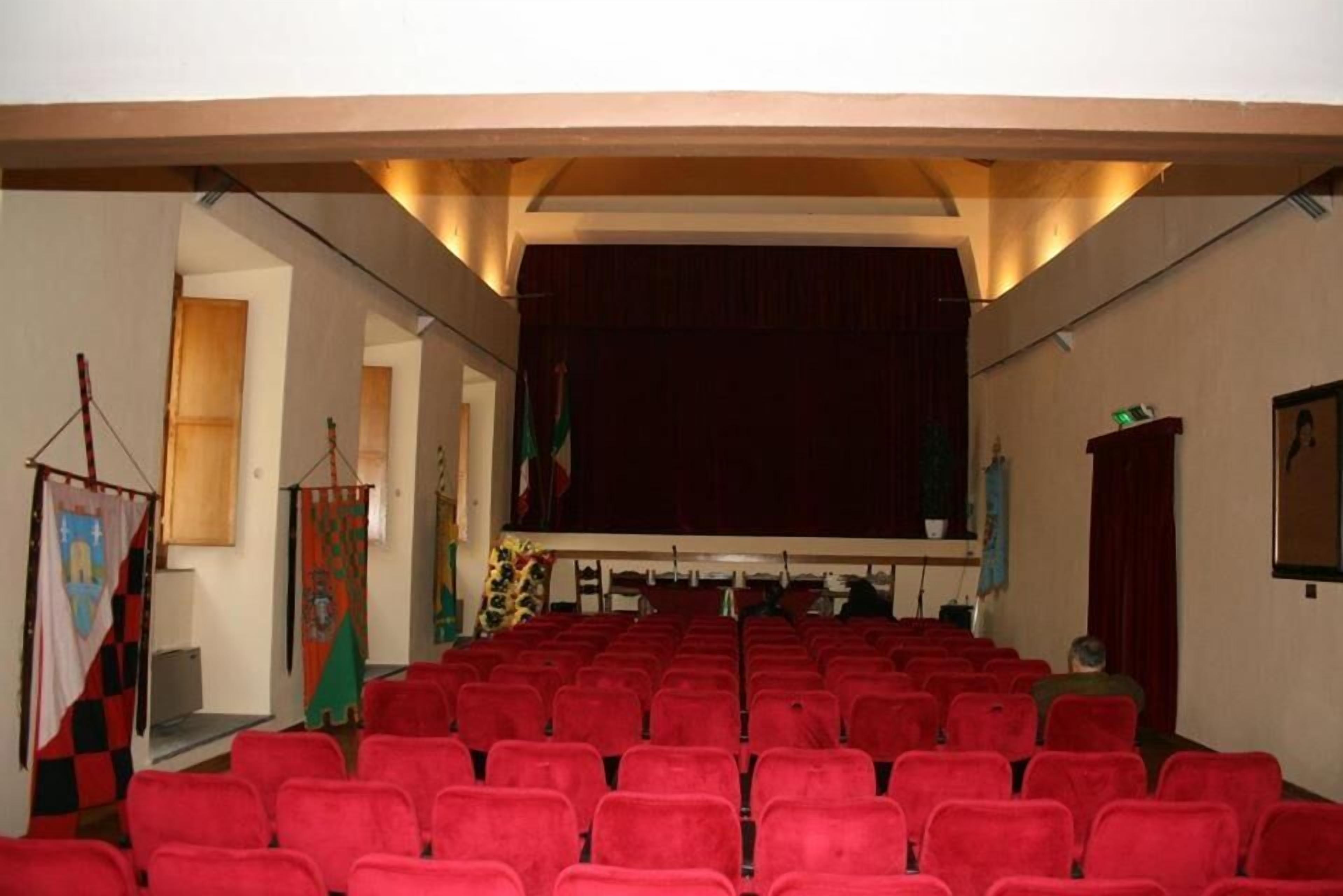 A theater with red chairs, a stage, and a balcony.