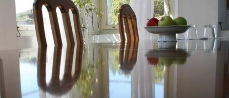 Una mesa de comedor con sillas, un cuenco de fruta y una planta junto a una ventana.