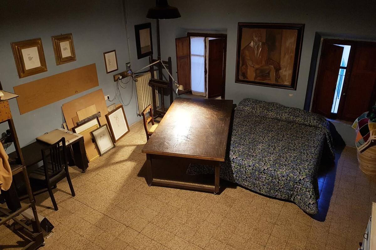 Une pièce comprenant un lit, un bureau et une chaise. Les murs sont ornés de tableaux encadrés et un grand tableau est accroché au-dessus du lit.