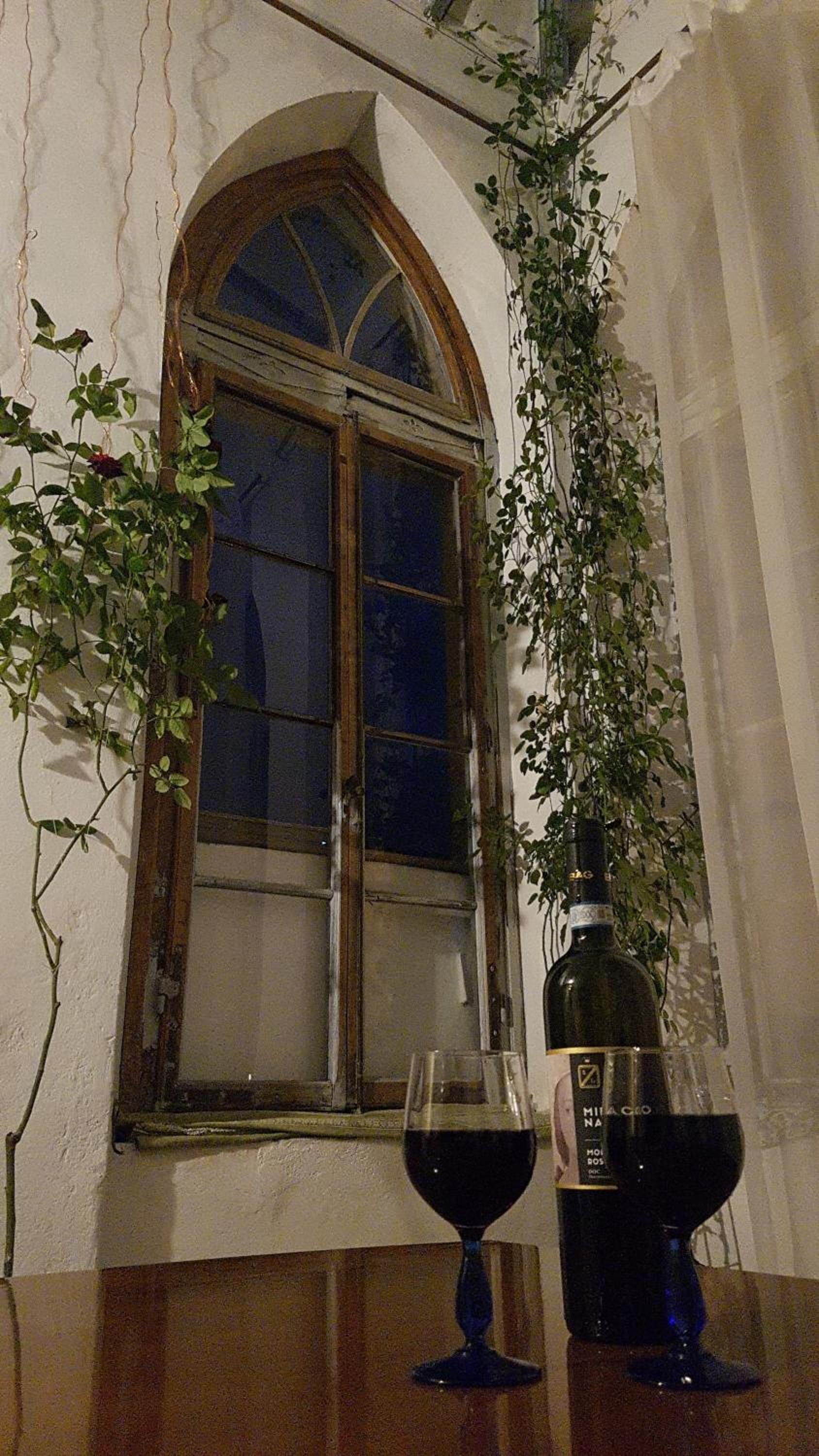 Una habitación rústica con una mesa de madera, un ventanal con marco de madera y una botella de vino.