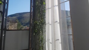 Um quarto com duas janelas em arco, uma com vista para uma paisagem montanhosa e a outra para um edifício.