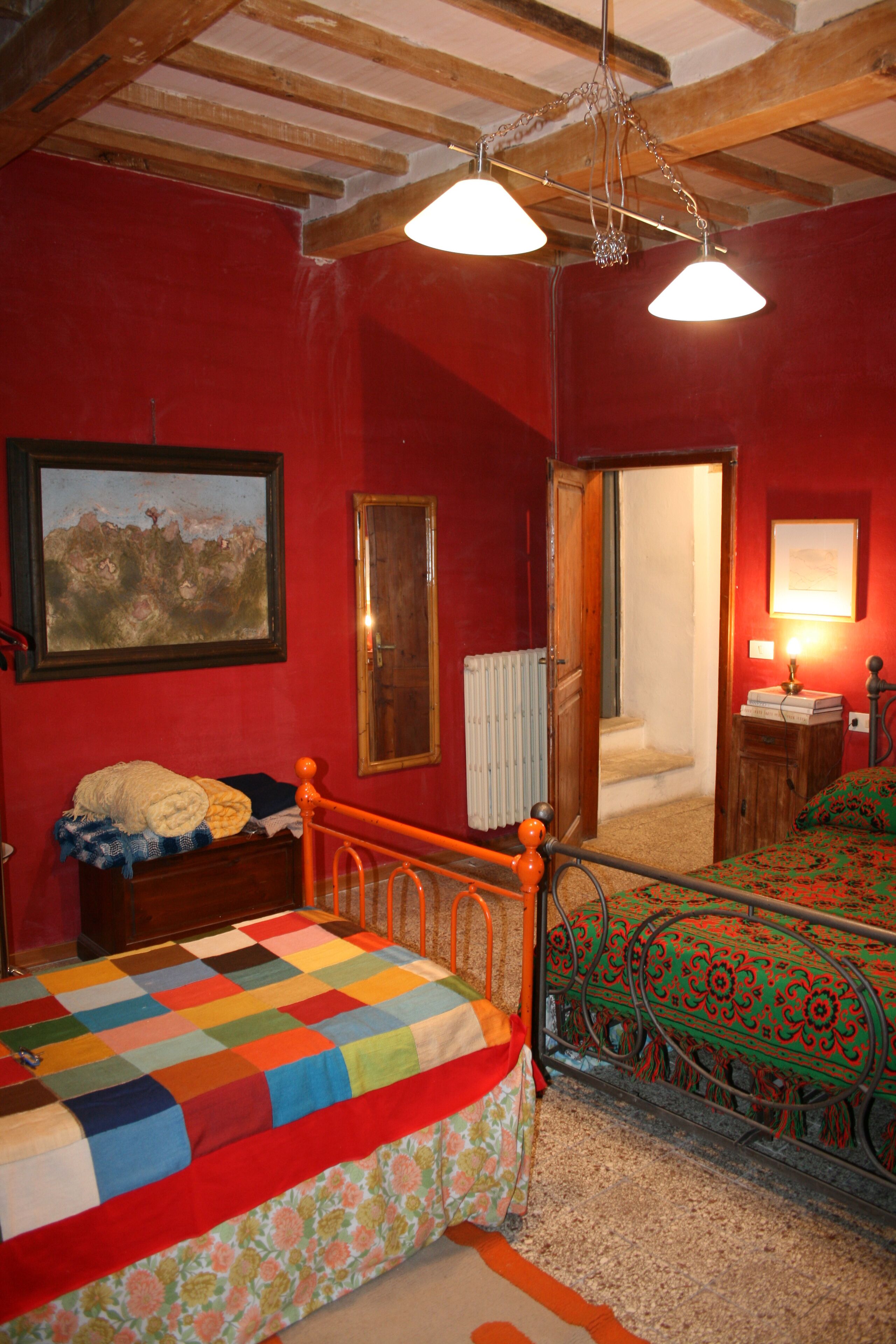 Una camera da letto con un letto a struttura in legno, una coperta colorata, una parete rossa, un quadro e una porta che dà su un'altra stanza.
