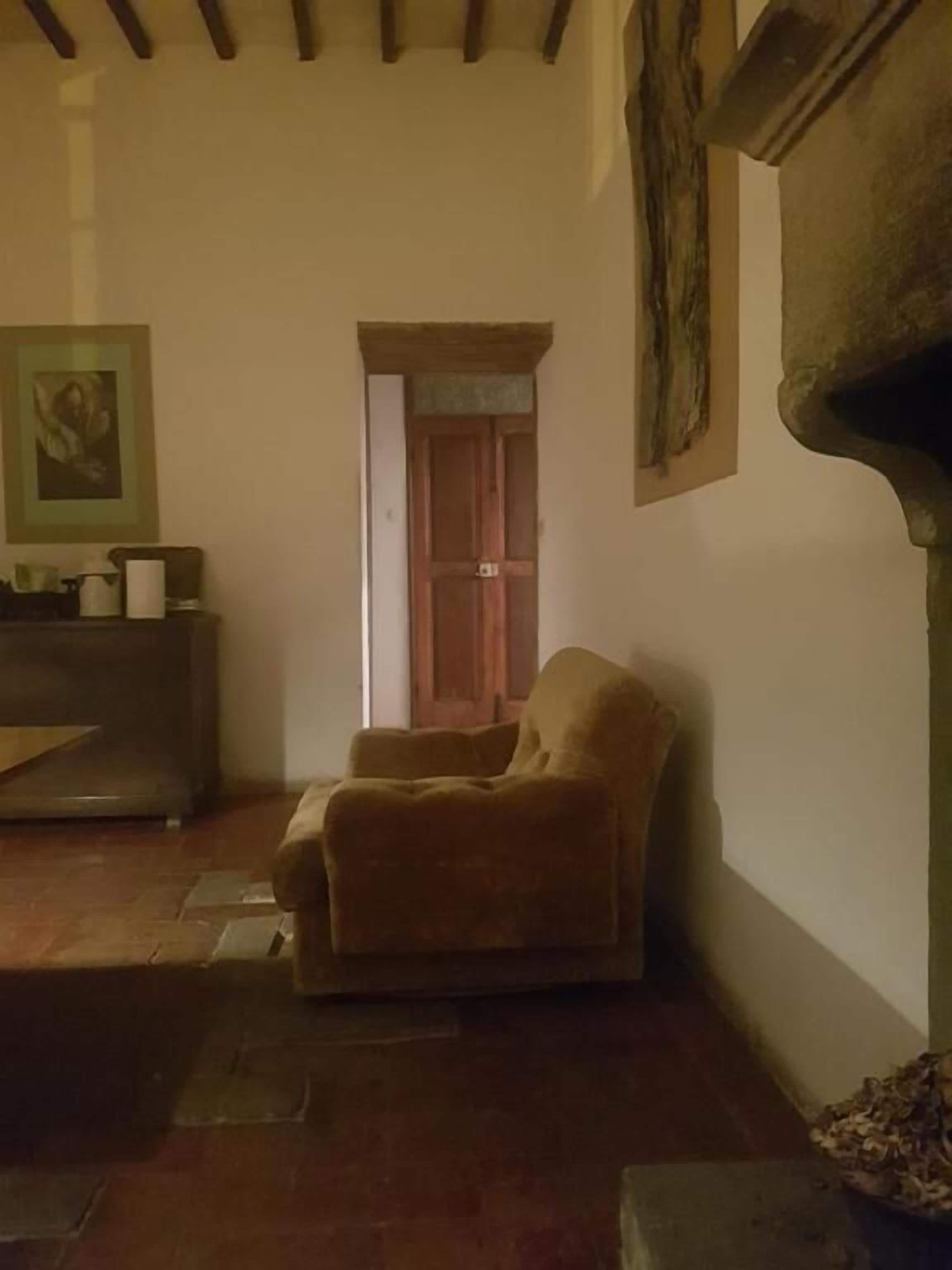 Una habitación con una silla de madera, una puerta, un cuadro enmarcado en la pared y una chimenea.
