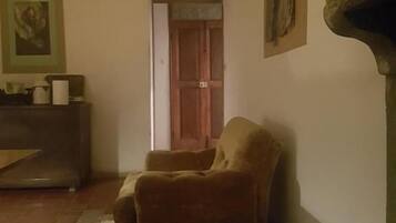 Una habitación con una silla de madera, una puerta, un cuadro enmarcado en la pared y una chimenea.