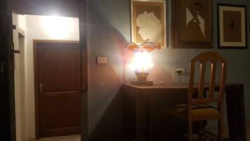 A room with a wooden door, a desk with a lamp, and framed artwork on the wall.