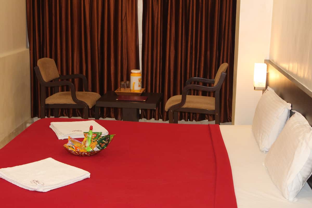 A hotel room with a bed, two chairs, a small table with a tray, and a lamp.